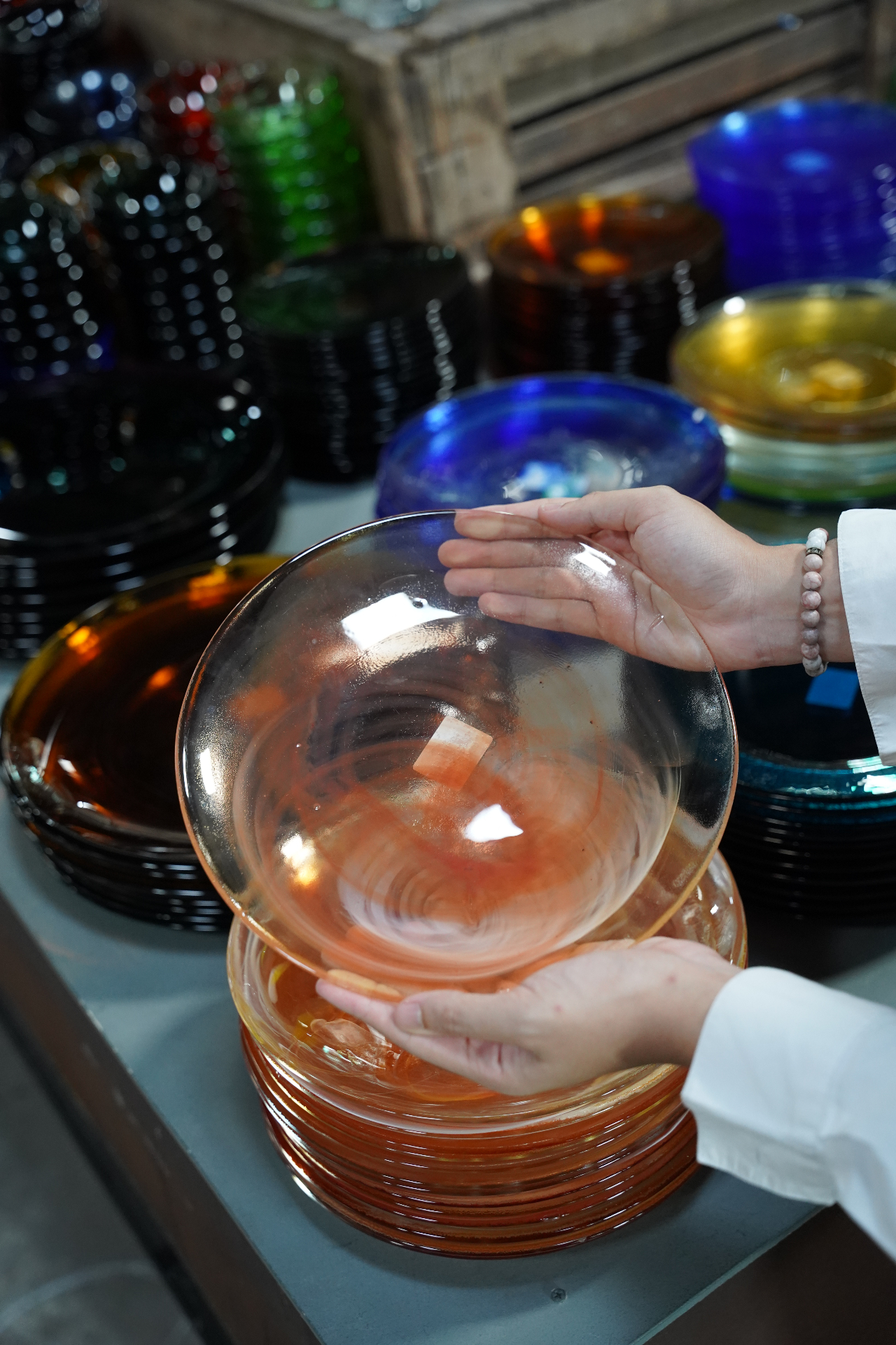 Amber handmade glass bowl held above stacks of coloured glass plates