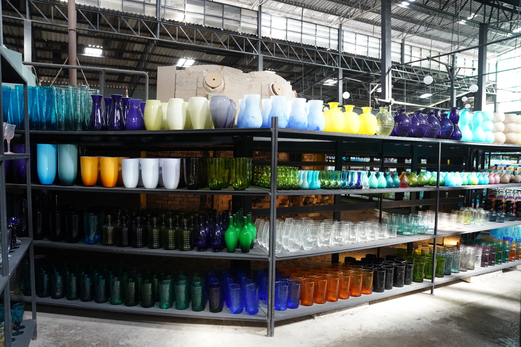 Rainbow rows of handmade glass vases, cups and tumblers on industrial shelving