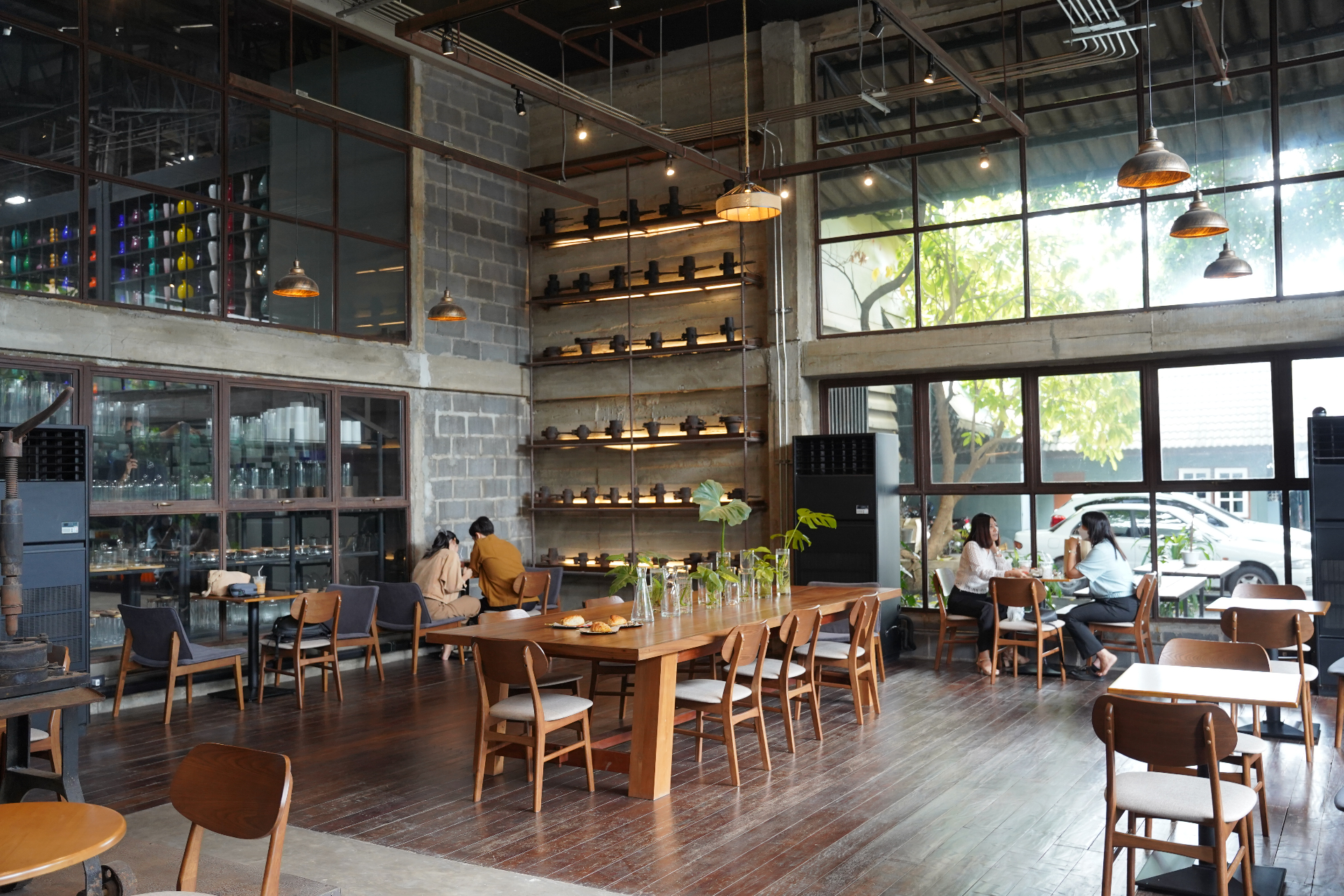 Eastern Glass garden café interior with long wooden communal table, glass display shelves and tropical light